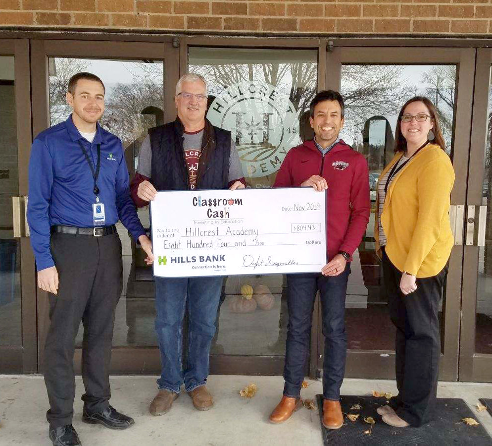 Tyler Coblentz (left) and Katie Miller (right) from Hills Bank present Hillcrest Academy Principal Dwight Gingerich (second from left) and Director of Advancement Jeremy Ours with a Classroom Cash check for $804.43.